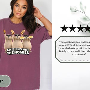 K&ouml;nnte beinhalten: Beerenfarbenes T-Shirt mit einer Grafik von drei Zeichentieren, die Sonnenbrillen tragen und Essen halten, mit dem Text "CHILLING WITH THE HOMIES". Das Shirt hat eine lockere Passform.