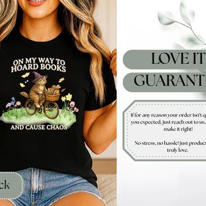 May include: Black t-shirt featuring a whimsical illustration of a cat riding a bicycle, wearing a witch hat, and carrying books. The text reads "ON MY WAY TO HOARD BOOKS AND CAUSE CHAOS".
