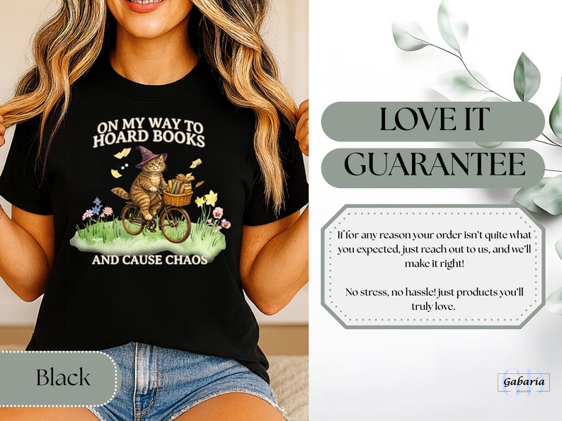 May include: Black t-shirt featuring a whimsical illustration of a cat riding a bicycle, wearing a witch hat, and carrying books. The text reads "ON MY WAY TO HOARD BOOKS AND CAUSE CHAOS".
