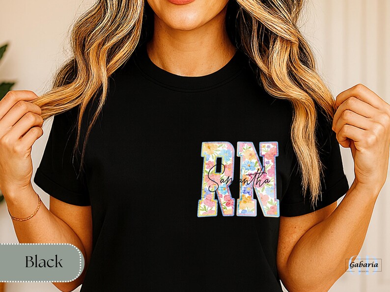 May include: Black t-shirt featuring the letters "RN" in a floral design, with the name "Samantha" in script below. The shirt is a crew neck style.