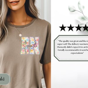 May include: Khaki-colored t-shirt featuring the letters "RN" filled with a floral design and the name "Samantha" in script. The shirt is a neutral color and has a round neckline. The image also includes a customer review.