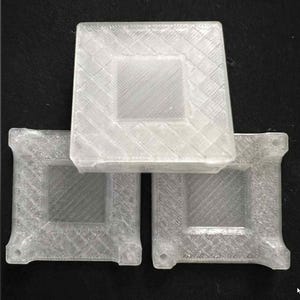 Peut inclure: Trois objets translucides de forme carrée sont empilés. Chaque objet présente un centre carré en relief et un motif texturé en croisillons sur la surface supérieure. Les objets ont de petites protubérances arrondies aux coins.