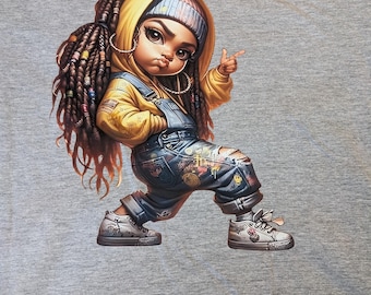 May include: A gray t-shirt featuring a cartoon illustration of a young person in a yellow hoodie and denim overalls. The character has long braids, hoop earrings, and sneakers, with a finger pointed forward.