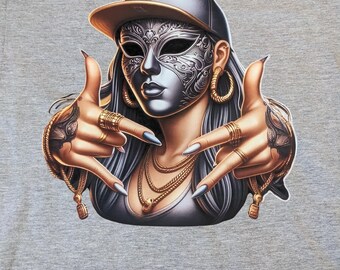 May include: Gray t-shirt featuring a detailed illustration of a person wearing a silver mask, a black baseball cap, and gold jewelry. The person is making hand gestures. The design has a hip-hop theme.