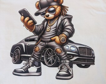 May include: White t-shirt featuring a cartoon bear wearing sunglasses, a cap, and gold jewelry, holding a phone. The bear is standing in front of a black car, wearing ripped jeans and sneakers. The bear has dreadlocks.