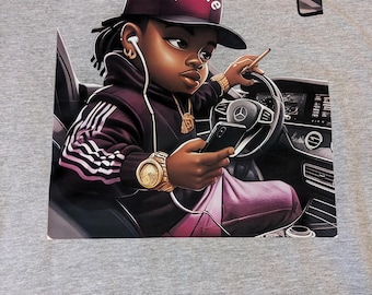 May include: A gray t-shirt featuring a cartoon illustration of a person in a car. The person wears a maroon cap with "B-More" text, a matching jacket with white stripes, and gold accessories. They hold a phone and a lit object.