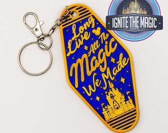 May include: A blue and gold keychain with the text "Long Live All The Magic We Made" and a castle illustration. The keychain has a metal clasp and ring. The design includes the text "IGNITE THE MAGIC DESIGN CO."