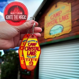 May include: Two yellow and red Camp Crystal Lake keychains with the text "WELCOME TO CAMP CRYSTAL LAKE EST. 1935 CABIN 13". A red circular sticker with the text "IGNITE THE MAGIC" is also visible.