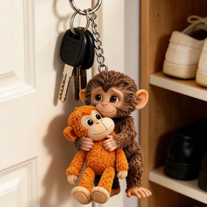 May include: A keychain featuring two monkey figurines. One brown monkey hugs an orange monkey. The keychain is attached to a silver ring with keys. The background shows a white door and a wooden shelf with shoes.