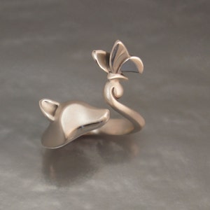 May include: A silver-toned ring featuring a fox head and a stylized flower. The fox head is on one end, while the flower sits atop a curved stem. The ring has a polished finish and a nature-inspired design.