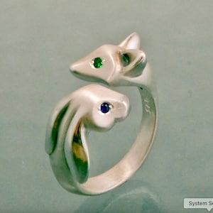 May include: A silver ring with a fox and rabbit design. The fox has a green gemstone eye, and the rabbit has a blue gemstone eye. A distinctive piece of jewellery.