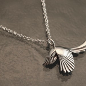 May include: A silver bird pendant necklace. The pendant is a stylized bird in flight, with detailed wing and tail feathers. The necklace chain is a delicate silver link. The bird pendant is approximately 1.5 inches long.