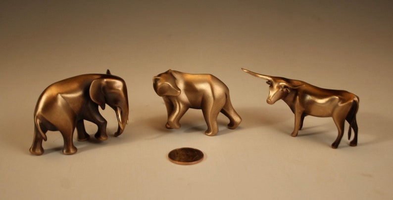 Puede incluir: Tres esculturas de animales de bronce: un elefante, un oso y un toro. El elefante y el oso caminan, mientras que el toro est&aacute; de pie con la cabeza levantada. Una moneda est&aacute; en el suelo frente a las esculturas.