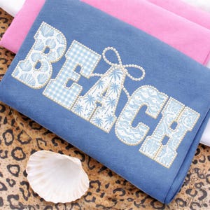 Pode incluir: Um tecido azul com a palavra "BEACH" em branco e azul claro, decorado com conchas, xadrez vichy, palmeiras e padrões de ondas. As letras são contornadas com pequenas contas peroladas. Uma concha marinha repousa sobre uma superfície com estampa de leopardo.