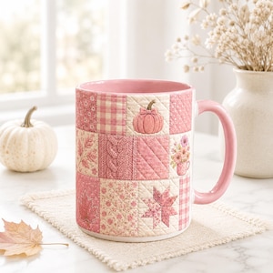 May include: A ceramic mug featuring a pink patchwork quilt design with various patterns including a pumpkin, cable knit texture, floral prints, gingham checks, and autumn leaves. The mug has a solid pink handle and a light pink interior finish.