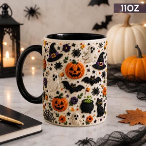 May include: A white ceramic mug with a black handle and interior, featuring a repeating pattern of embroidered-style Halloween icons including orange jack-o'-lanterns, white ghosts, black bats, spiders, a black cat, and a cauldron. Text reads 11OZ.