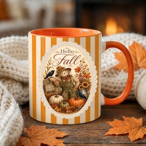 May include: A ceramic mug with orange and white vertical stripes, an orange interior, and an orange handle. The front features an oval illustration of a scarecrow, pumpkins, sunflowers, and black birds with the text Hello Fall and Grateful Thankful Blessed.