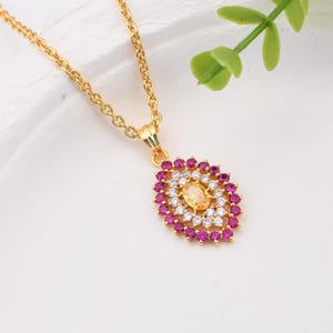 May include: A gold chain necklace featuring an oval pendant. The pendant has a central oval yellow gemstone surrounded by a halo of small white stones, which is further encircled by an outer border of small, vibrant pink circular gemstones.