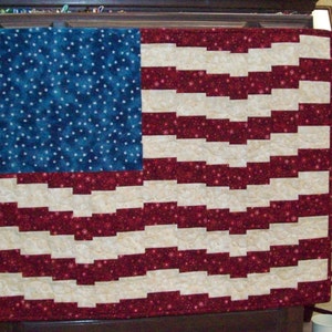 May include: A red, white, and blue patchwork quilt with a zig-zag pattern. The quilt is made of fabric with a white star pattern on the blue section.