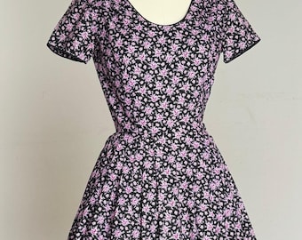 May include: A vintage-style dress with a black background and a repeating pattern of small pink flowers. The dress has a scoop neckline, short sleeves, and a full skirt. The dress is displayed on a mannequin.