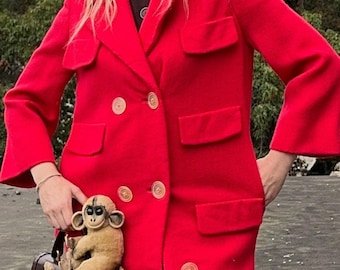 May include: A bright red double-breasted coat with large buttons and pockets. A brown leather handbag is adorned with a stuffed monkey. The coat has a classic design with a tailored fit.