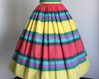May include: A full circle skirt with a colorful striped pattern in shades of red, yellow, green, blue, and purple. The skirt is made of a lightweight fabric and has a gathered waist.