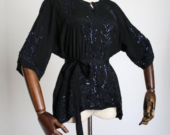 May include: A black silk blouse with a tie belt and blue beaded embroidery. The embroidery features a floral design.