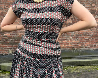May include: A black and white dress with red and green geometric patterns. The dress has a fitted bodice and a full skirt.
