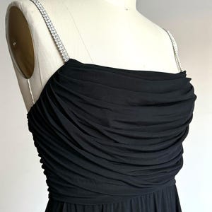 May include: A black strapless dress with a ruched bodice and a flowing skirt. The straps are adorned with a rhinestone trim.