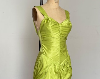 May include: A sleeveless lime green satin top featuring a sweetheart neckline, wide shoulder straps, and vertical ruching along the bodice. The garment has a V-shaped waist seam with gathered fabric at the lower section, creating a soft, draped effect.