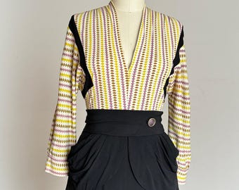 以下が含まれることがあります： ヴィンテージのツーピースドレス。トップは柄入り、ボトムは黒。トップはVネックと長袖で、黄色、紫、茶色の形の繰り返し模様。黒いスカートはハイウエストで、ユニークなポケットのディテールが特徴です。