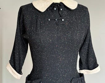 May include: A black dress with a white collar and black buttons. The dress has a speckled pattern and 3/4 sleeves.