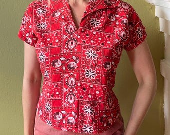 May include: A short-sleeved button-down shirt in a vibrant red color featuring a repeating white and black bandana-style print. The pattern consists of alternating square panels with floral motifs, paisley-like shapes, and geometric borders.