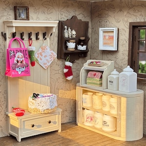 May include: Miniature dollhouse kitchen scene with a pink Barbie Girl tote bag hanging on a coat rack. A small bench holds a basket and a red strawberry. Shelves display jars, a breadbox, and canisters.
