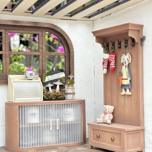 May include: A miniature dollhouse interior scene featuring a wooden cabinet, a coat rack with decorative items, and a small bench. The scene includes a teddy bear, a bunny figurine, and a sign that reads "T. Magee, Druggist."