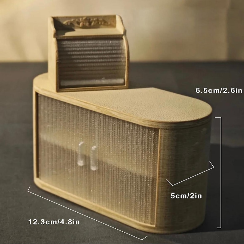 May include: A miniature wooden cabinet with a light brown finish. The cabinet has a curved design with a textured, semi-transparent front. It measures 4.8 inches wide, 2 inches deep, and 2.6 inches tall. A smaller, matching top piece is attached.
