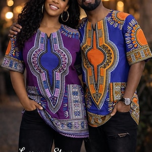 May include: Two short-sleeved shirts featuring intricate dashiki-style patterns. One shirt is primarily purple with blue, white, and black accents, while the other is blue with orange, yellow, and black details. Both have round necklines.