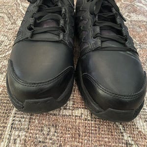 May include: A pair of black leather sneakers with black laces. The shoes have a textured design on the sides and a black rubber sole.