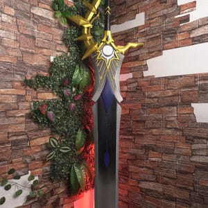 May include: A large, ornate sword with a gold hilt and accents, a gray blade, and a blue and black handle. The sword is displayed against a brick wall with greenery.