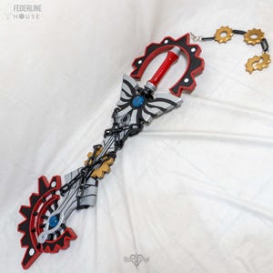 May include: A detailed prop keyblade with a red handle and accents, black and red gear-shaped designs, and silver and blue details. The keyblade has a chain with gold gears attached. The Federline House logo is in the top left corner.