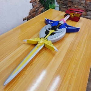 May include: A detailed, colorful toy sword with a silver blade and yellow accents. The hilt features a red handle, a pink section, and blue and yellow decorative elements. The sword is set against a wooden surface.