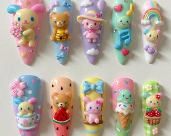 Könnte beinhalten: Zehn künstliche Fingernägel, jeweils individuell mit farbenfrohen Cartoon-Designs verziert. Die Nägel zeigen verschiedene Themen wie Bären, Hasen, Regenbogen, Noten und Eiswaffeln. Pastellfarben und 3D-Verzierungen sorgen für eine verspielte Ästhetik.