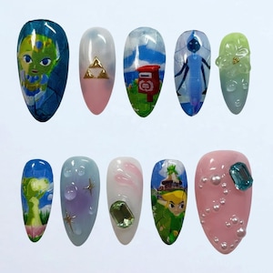 May include: A set of ten almond-shaped artificial nails, each with a unique design. The designs include cartoon characters, gold triangles, a red mailbox, and abstract patterns. Colors include blue, pink, green, and white.