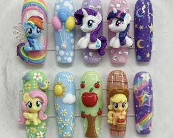 Puede incluir: Un conjunto de doce uñas artificiales, cada una diseñada de forma única con personajes coloridos de My Little Pony y fondos temáticos. Los diseños incluyen arcoíris, globos, estrellas y manzanas, con una variedad de colores y texturas.