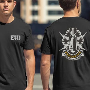 May include: Black t-shirts with white graphics. One shirt features "EOD" in a block font on the front. The other shirt displays a bomb graphic with the words "EXPLOSIVE ORDNANCE DISPOSAL" on the back. The design includes lightning bolts and a star.