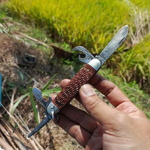 Peut inclure: Un couteau de poche multi-outils doté d'un manche marron texturé avec un motif quadrillé. Le couteau comprend une lame pliante principale, un décapsuleur et deux outils métalliques supplémentaires s'étendant aux extrémités, tous en métal.