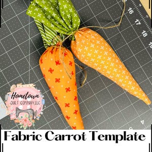 May include: Two fabric carrots, one orange with a white star pattern and one green with a white star pattern, tied together with twine. The carrots are on a gray cutting mat with white grid lines. The text "Fabric Carrot Template" is at the bottom of the image.