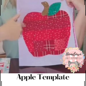 Op de afbeelding: Een rode appel sjabloon met een groen blad en een gouden steel, gemaakt van verschillende stofpatronen. Het sjabloon wordt omhoog gehouden, waarbij het ontwerp wordt getoond. De tekst "Apple Template" staat eronder.