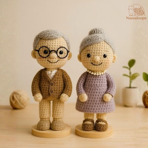 K&ouml;nnte beinhalten: Geh&auml;kelte Puppen eines &auml;lteren Ehepaares. Die m&auml;nnliche Puppe tr&auml;gt eine braune Jacke, eine Brille und ein wei&szlig;es Hemd. Die weibliche Puppe tr&auml;gt ein lila Kleid und eine Perlenkette. Beide Puppen haben graues Haar und stehen auf Holzsockeln.