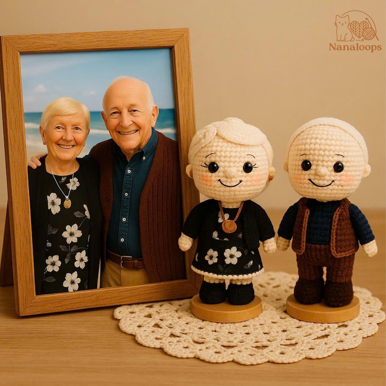 K&ouml;nnte beinhalten: Ein gerahmtes Foto eines &auml;lteren Ehepaares steht neben zwei geh&auml;kelten Puppen. Die Puppen tragen Miniatur-Outfits, und die Puppen-Frau tr&auml;gt ein schwarzes Kleid mit wei&szlig;en Blumenmustern.